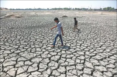  ?? AJIT SOLANKI / ASSOCIATED PRESS ?? Indian boys on their way to play cricket walk through a dried patch of Chandola Lake in Ahmadabad, India. Much of the country has been suffering from a heat wave for weeks along with a severe drought that has decimated crops, killed livestock and left...