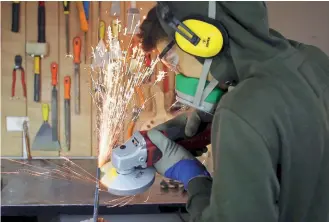  ??  ?? Wearing special gloves, headphones and a mask, 14-year-old Yiannis cuts and polishes an iron knife he’s making.