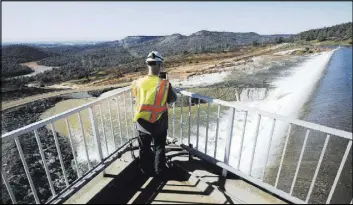  ?? RICH PEDRONCELL­I/THE ASSOCIATED PRESS ?? Jason Newton of the Department of Water Resources takes a picture Saturday of water going over the emergency spillway at Oroville Dam in Oroville, Calif. Water started flowing over the emergency spillway at the nation’s tallest dam for the first time...