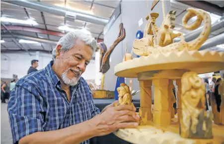  ?? PHOTOS BY GABRIELA CAMPOS THE NEW MEXICAN ?? Carlos Santisteva­n of Denver makes an adjustment to the placement of his first-place wood carving, Batalla De San Jorge, at the Spanish Market preview Friday evening at El Museo Cultural.