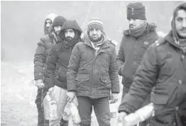  ?? LEONID SHCHEGLOV/BELTA ?? Migrants line up to collect drinking water as they gather Friday at the Belarus-Poland border near Grodno, Belarus.