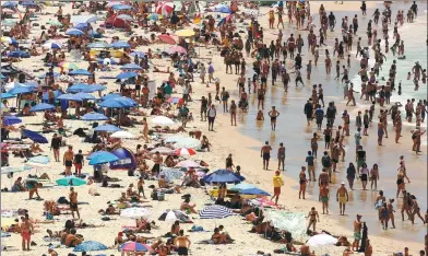  ?? GLENN CAMPBELL / AAP VIA REUTERS ?? Beachgoers sit on the sand and walk in the water at Sydney's Bondi Beach on a hot summer day on Sunday.