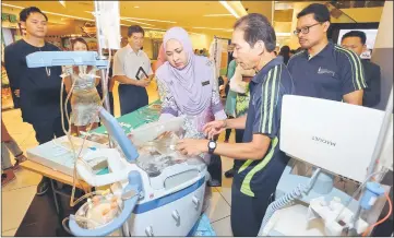  ??  ?? Dr Jamilah takes a closer look at a medical equipment on display at an exhibition booths in Sarawak Islamic Complex. Briefing her is Dr Hasmizy (right). — Photo by Muhammad Rais Sanusi