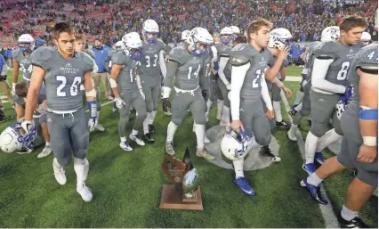  ?? MARK HOFFMAN / MILWAUKEE JOURNAL SENTINEL ?? Brookfield Central players walk past their runner-up trophy after falling, 14-13, to Waunakee in the Division 2 state football championsh­ip game. A WIAA official eventually handed the trophy to a member of the coaching staff.