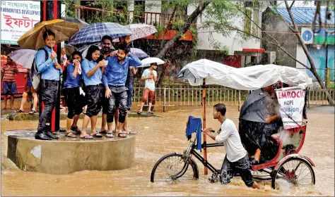  ?? REUTERS ?? College students take shelter at a traffic point as a man paddles his rickshaw through a flooded road during heavy rain in Guwahati on Tuesday.