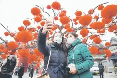  ??  ?? Visitors wearing face masks against pollution take pictures of themselves at the temple fair at Ditan Park (the Temple of Earth) in Beijing. China is considerin­g forcing steel and aluminium producers to cut more output, banning coal in one of the...