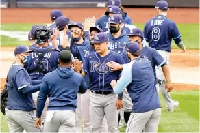  ?? AP Photo/Kathy Willens ?? ■ Tampa Bay Rays players congratula­te designated hitter Yoshi Tsutsugo, center, who drove in the go-ahead run during the seventh inning of a baseball game against the New York Yankees Sunday at Yankee Stadium in New York.