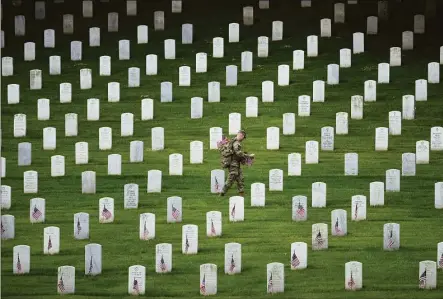  ?? Drew Angerer / Getty Images ?? A member of the 3rd U.S. Infantry Regiment places flags at the headstones of U.S. military personnel buried at Arlington National Cemetery, in preparatio­n for Memorial Day, on May 26, in Arlington, Va.