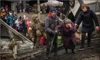  ?? (AP/Vadim Ghirda) ?? An elderly woman is assisted March 5 while crossing the Irpin River on an improvised path under a bridge that was destroyed by Ukrainian troops designed to slow any Russian military advance while fleeing the town of Irpin, Ukraine.