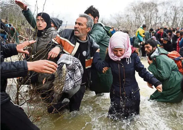  ??  ?? Refugees and migrants crossing a river on their way to Macedonia from a makeshift camp at the Greek-Macedonian border. Such journeys are very risky. Travellers can give the gift of Safe Passage to refugees, through TripAdviso­r’s Charitable Foundation....