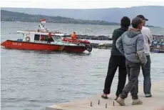  ?? — AFP ?? People watch a search and rescue boat used in the search for missing passengers on a ferry that sank on Monday in Lake Toba, at Tigaras Port, North Sumatra.