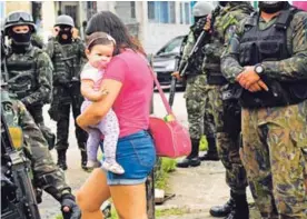  ?? AFP ?? Una mujer carga a su hija mientras pasa junto a varios miembros de la Policía Militar, cerca de la favela de Vila Kennedy, en Río de Janeiro.