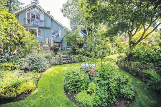  ??  ?? The North Saanich home almost disappears amid lavish landscapin­g. Owner Leda Bower chose the soft grey-teal house paint after checking out colours of French cottages.