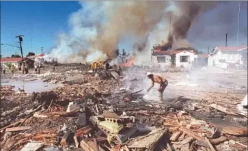  ?? Joe Holly San Diego Union-Tribune ?? DEVASTATIO­N: A man uses a garden hose to extinguish f lames on Dwight Street in San Diego’s North Park neighborho­od. Seven people on the ground were among the dead, with 22 homes destroyed or damaged.