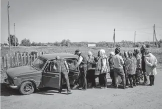  ?? Photos by Bernat Armangue/Associated Press ?? Villagers line up to buy cigarettes and bread from a peddler Friday in the village of Staryi Saltiv, east Kharkiv, Ukraine. The village is under constant Russian shelling.