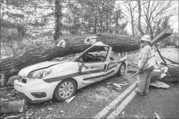  ?? Associated Press photo ?? An electrical worker for INTREN, a electric company from Chicago that drove two days to get to Philadelph­ia to help PECO restore power, walks by a damaged vehicle in Bryn Mawr, Pa., on Sunday that was crushed by a falling tree on Friday. The driver was...