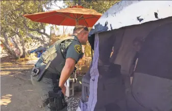  ?? Amy Taxin / Associated Press ?? An Orange County sheriff ’s deputy tells occupants of a tent in Anaheim that they need to leave and that the county will assist with the move. Some have lived in the encampment for years.